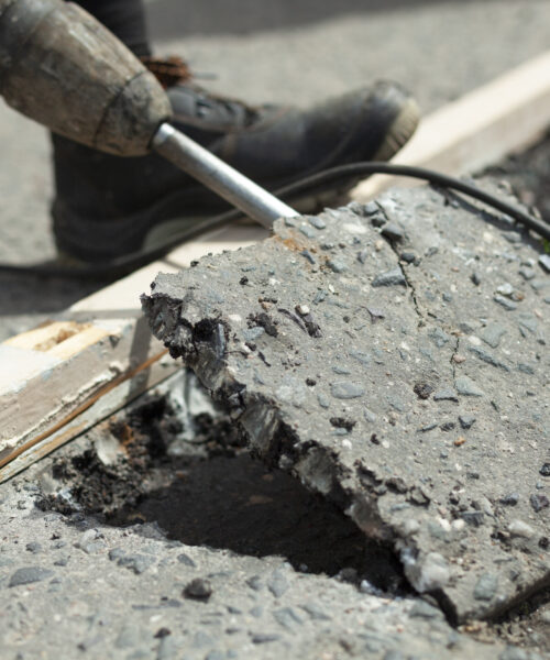 He removes the asphalt with a jackhammer. Removing the asphalt layer from the road. The worker holds a jackhammer. Road repair. Using an electric hammer.